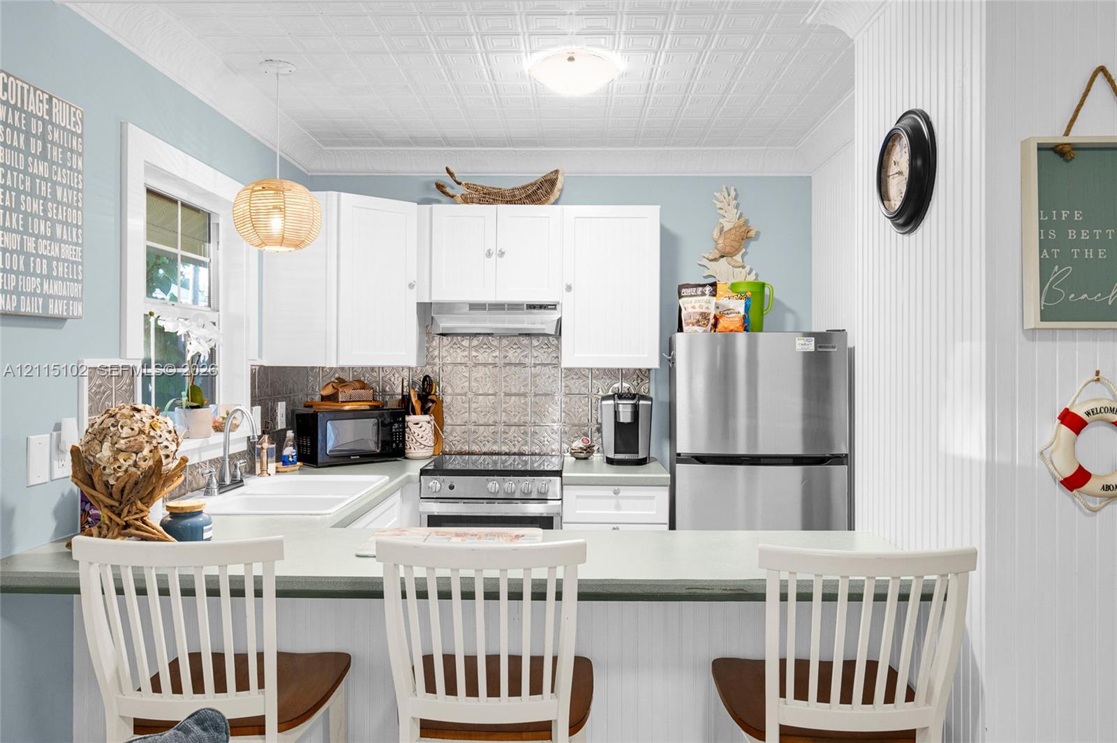 Kitchen featuring white cabinetry, metallic patterned backsplash, white farmhouse-style dual-basin sink, beadboard wall paneling, and a decorative pressed-tin style ceiling