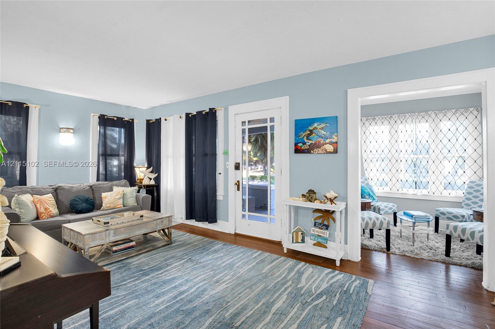 Living area featuring wood-finish flooring, a multi-pane glass entry door, and an archway leading to a secondary room with decorative lattice window film and wall-mounted lighting