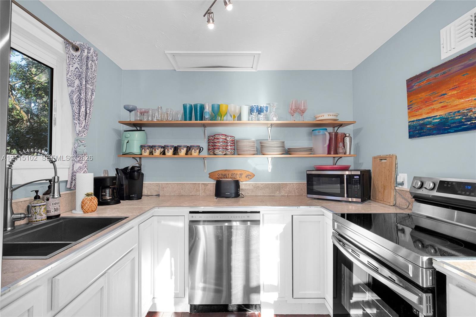 Kitchen featuring white cabinetry, solid surface countertops, dual stainless steel appliances, open wood shelving, and a double-basin undermount sink
