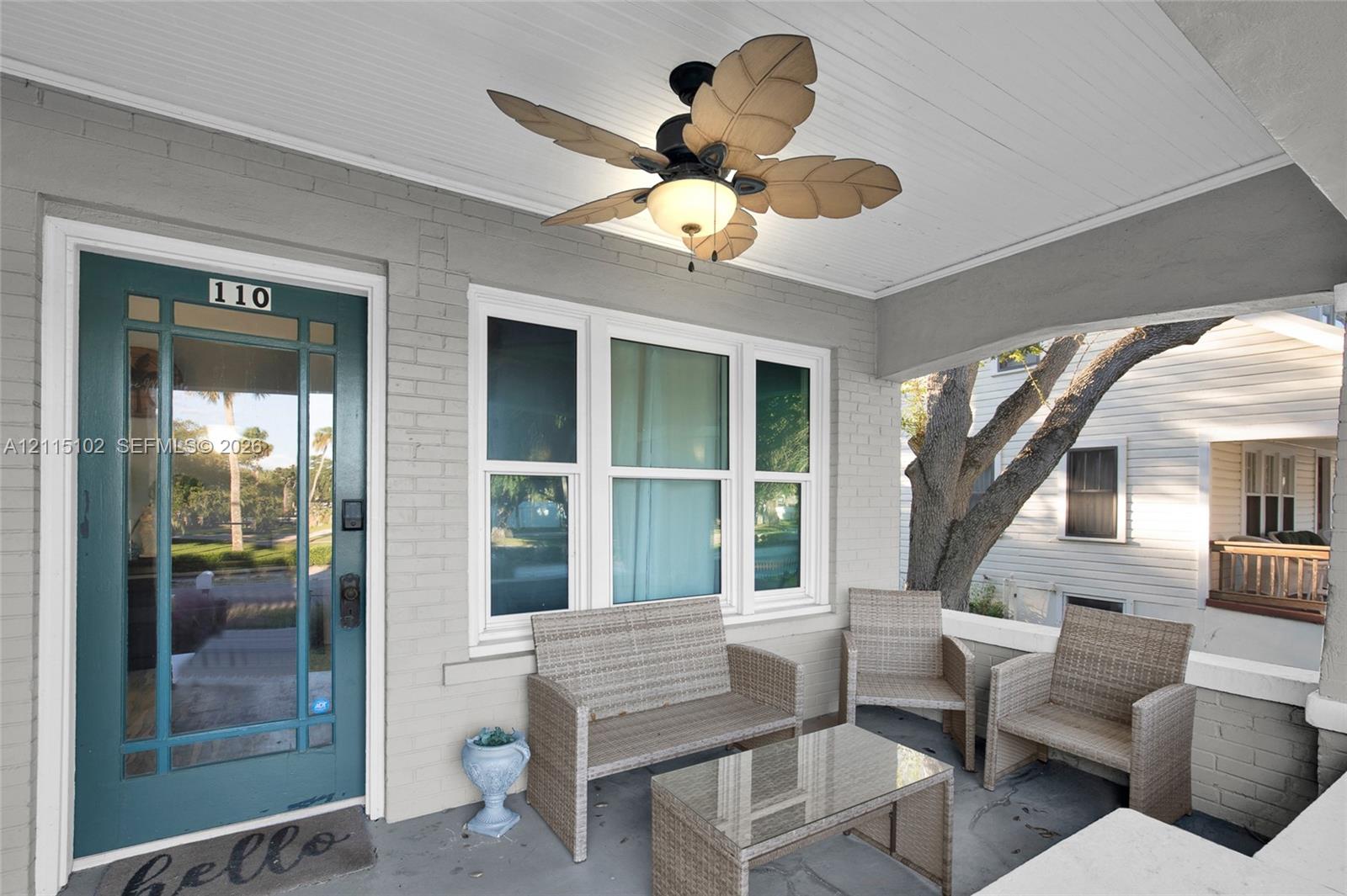 Covered front porch featuring a painted brick exterior, teal-finished glass-paneled entry door, beadboard ceiling, and integrated palm-leaf style ceiling fan