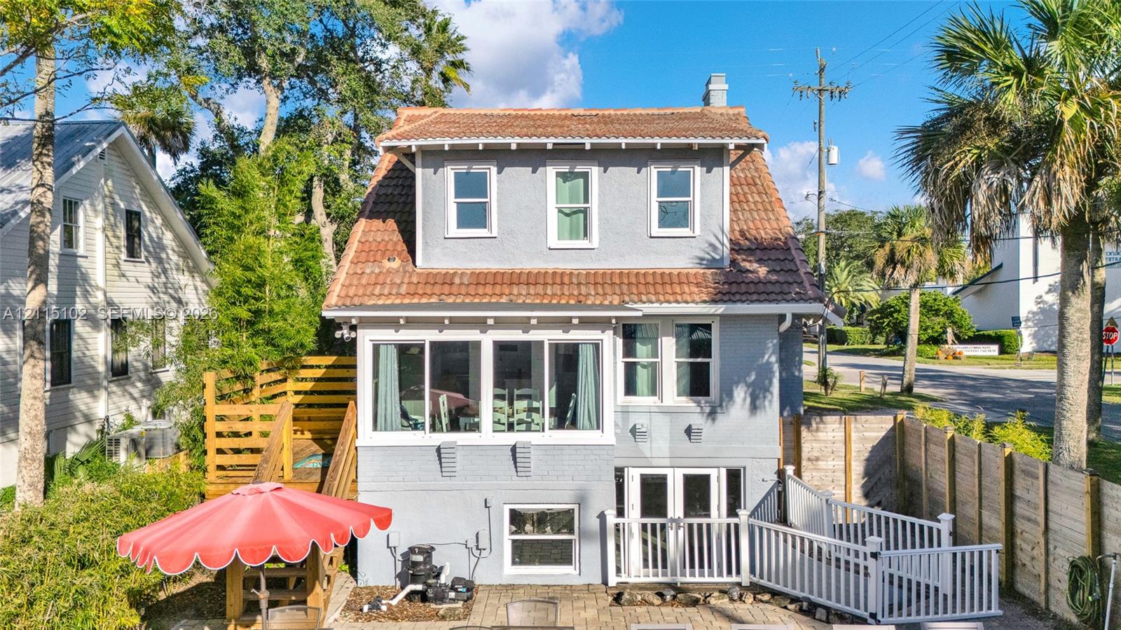 Multi-level exterior featuring a mansard roof, stucco siding, a glass-enclosed upper porch, and a paved ground-level patio with decorative fencing