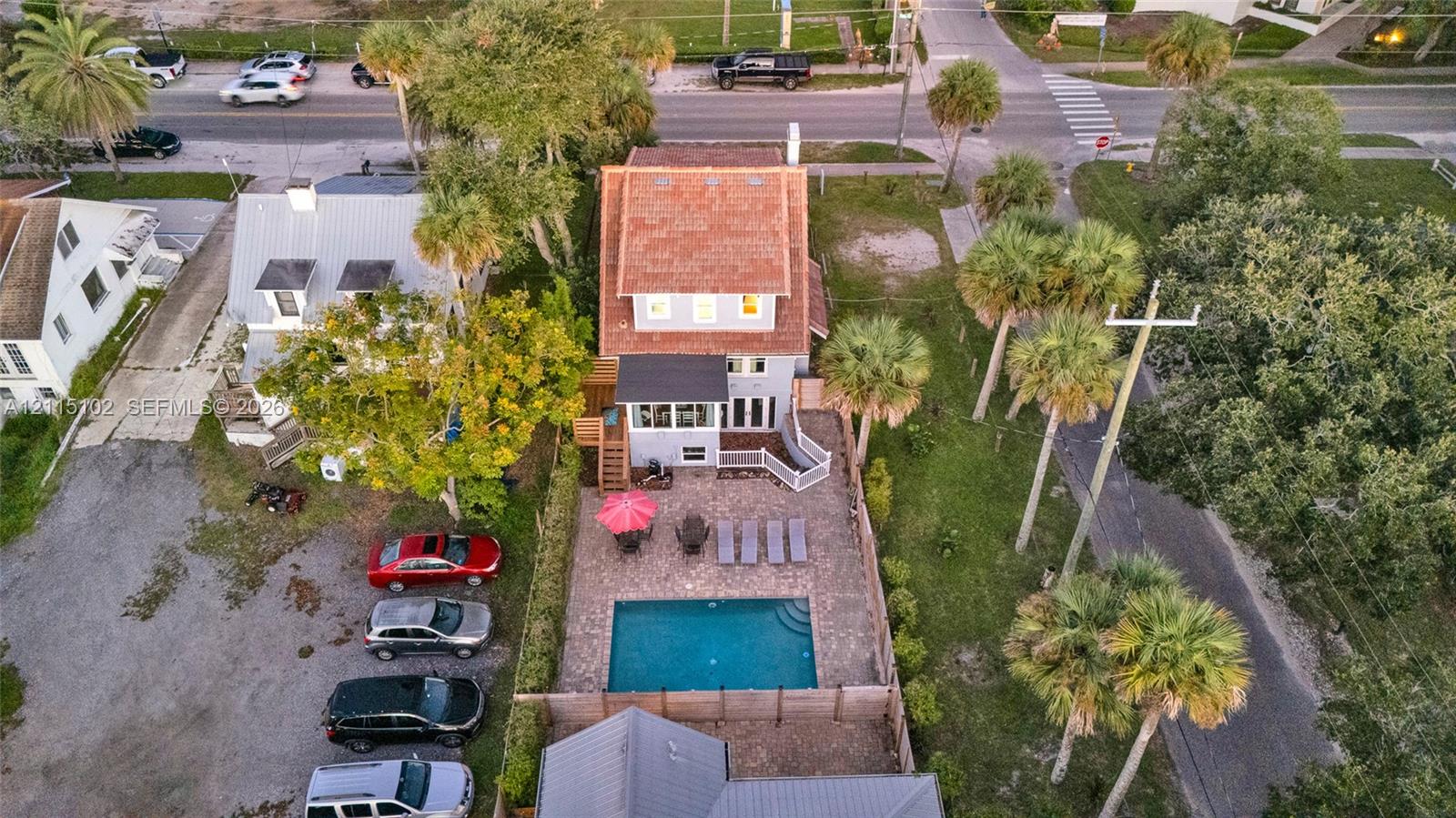 Aerial perspective of a multi-story residence featuring a shingled roof, a paved patio, an in-ground swimming pool, and mature palm trees