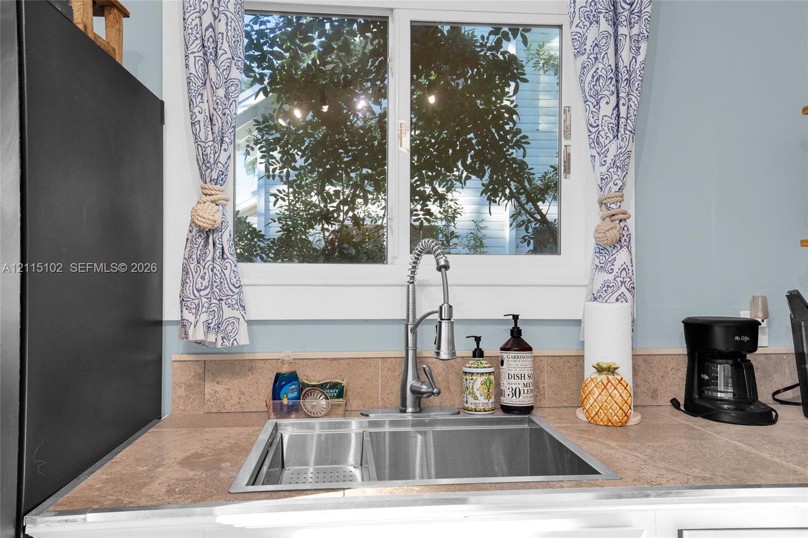 Stainless steel dual-basin undermount sink featuring a high-arc pull-down faucet and tile countertop