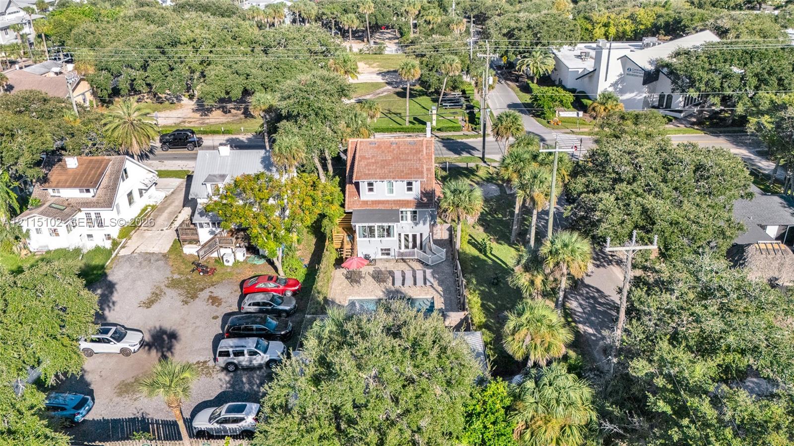 Aerial perspective featuring a multi-story residence with a pitched roof, an in-ground swimming pool, a stone-surfaced patio area, and mature canopy trees