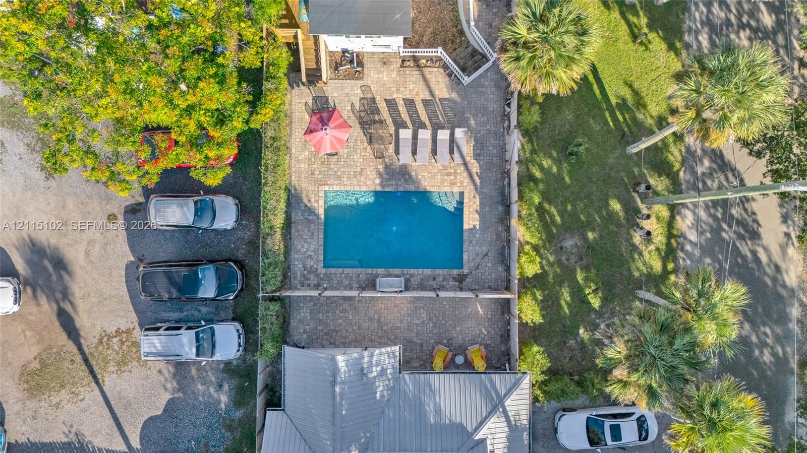Aerial perspective of an outdoor space featuring a rectangular in-ground swimming pool, stone paver decking, and mature palm trees