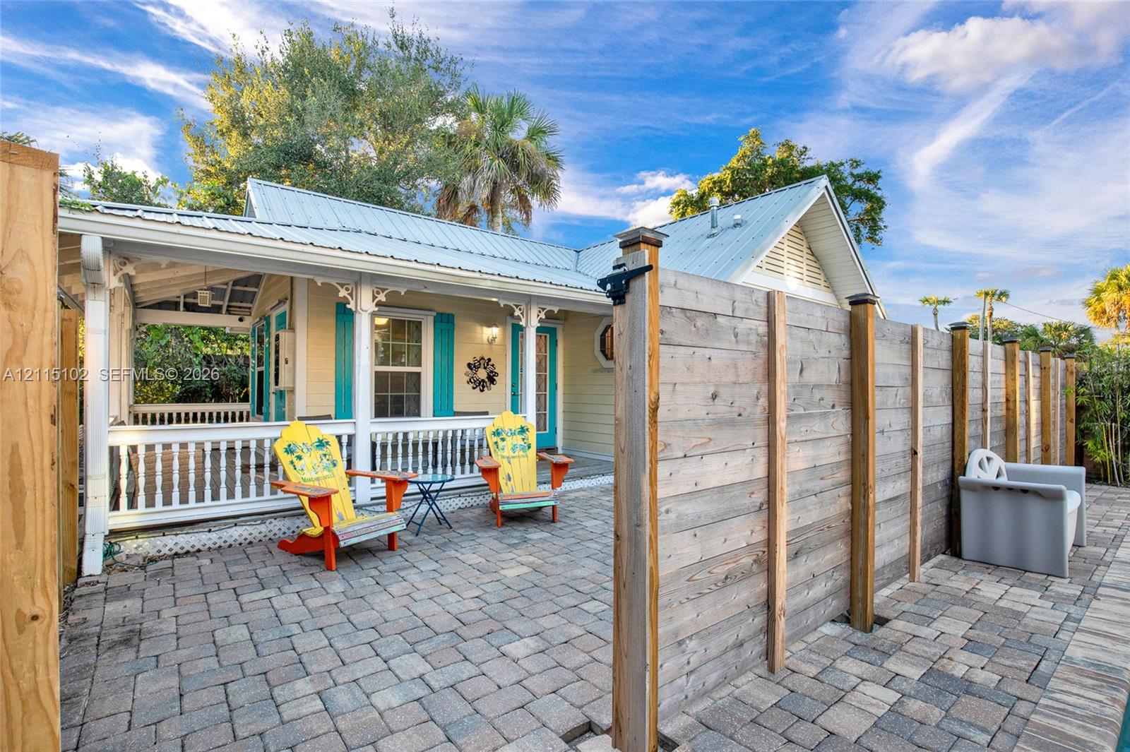 Paver patio area featuring a horizontal wood-plank privacy fence and a covered porch with decorative corbels and white balustrade railing