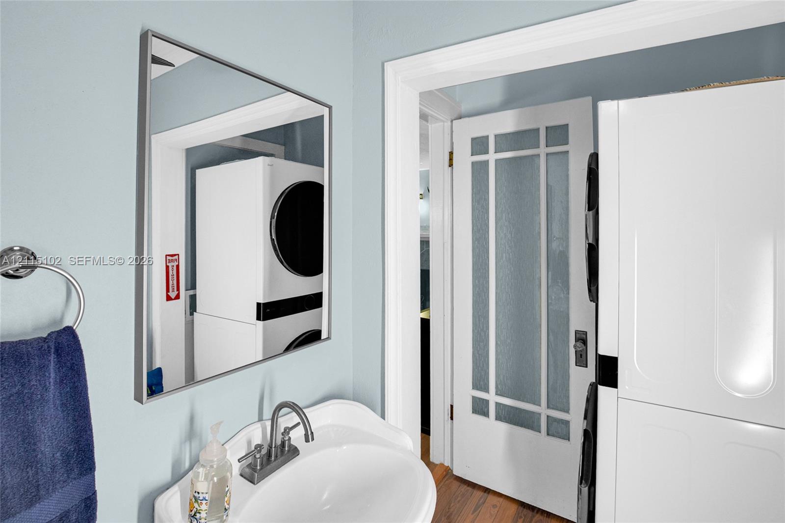 Pedestal sink with chrome-finish faucet, rectangular wall-mounted mirror, and white door featuring glass panels