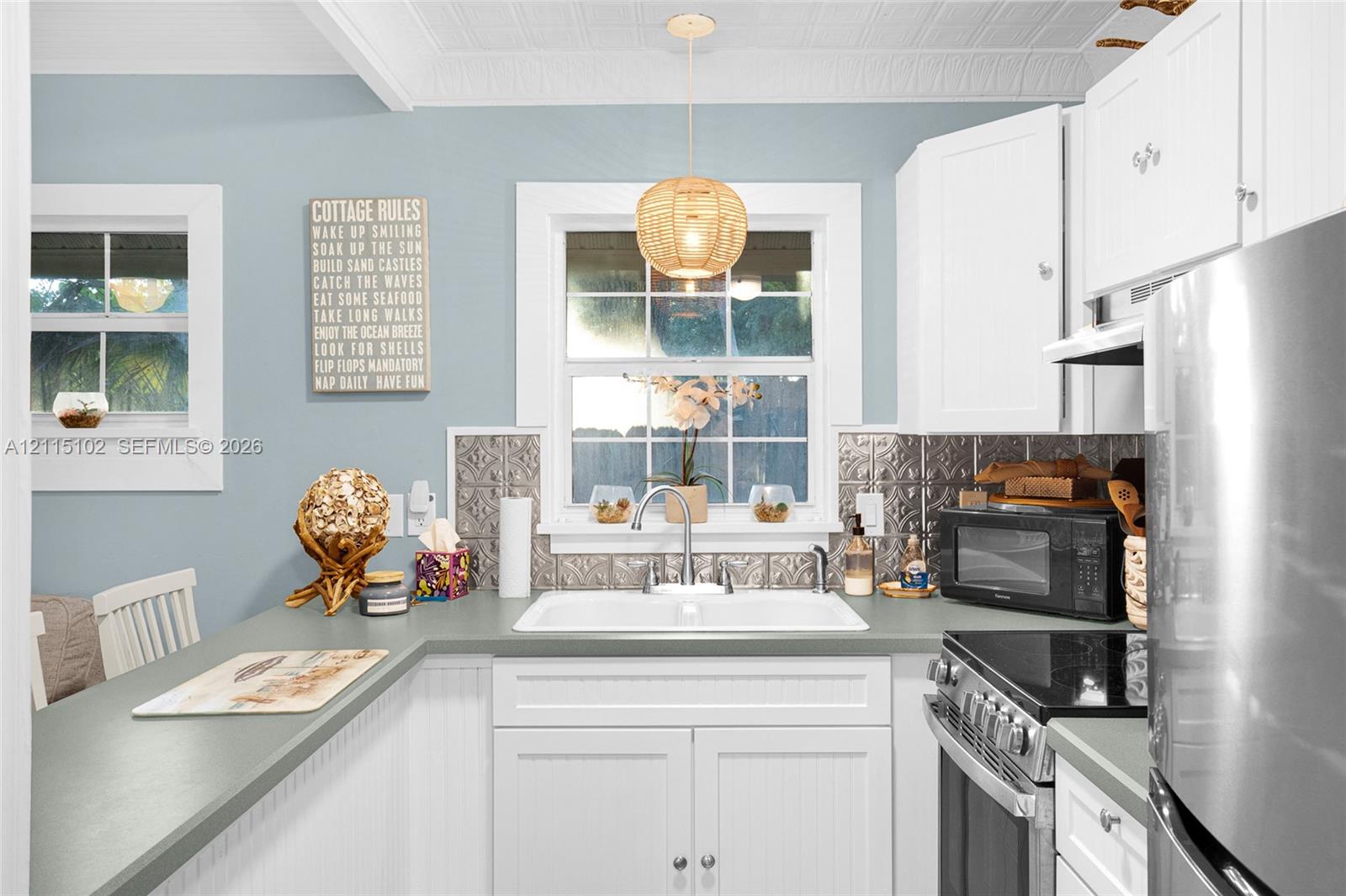 Kitchen featuring white beadboard cabinetry, metallic decorative backsplash, double-basin sink with gooseneck faucet, textured ceiling, and pendant lighting