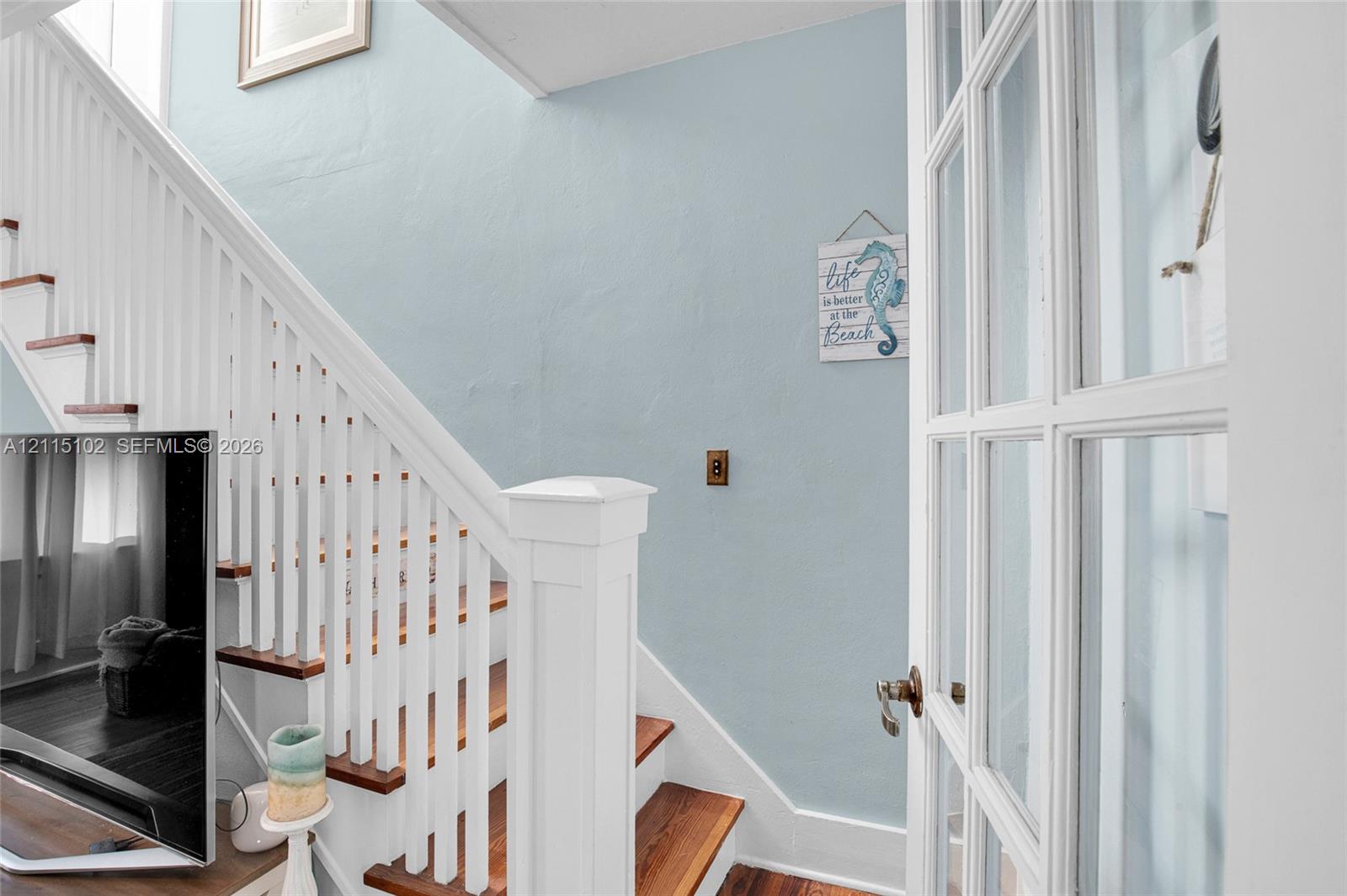 Staircase featuring wood-finish treads, a white balustrade with a prominent newel post, and an attached multi-pane French door