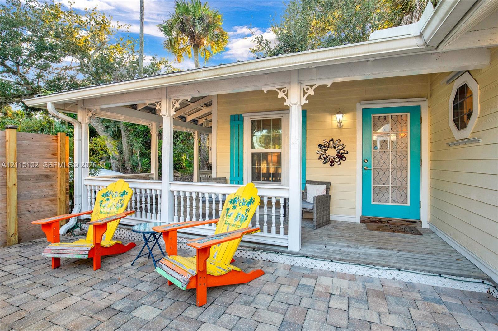 Covered porch featuring intricate gingerbread trim, horizontal lap siding, a paneled front door with divided-light glass, and a stone-paver patio