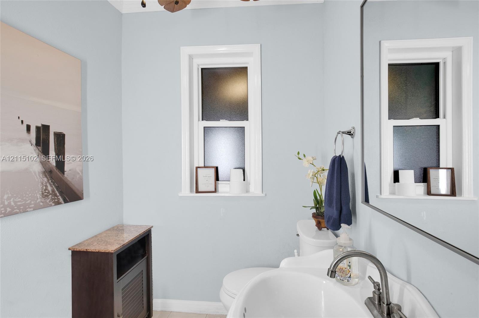 Bathroom featuring a pedestal sink, brushed-nickel faucet, framed mirror, and double-hung frosted windows
