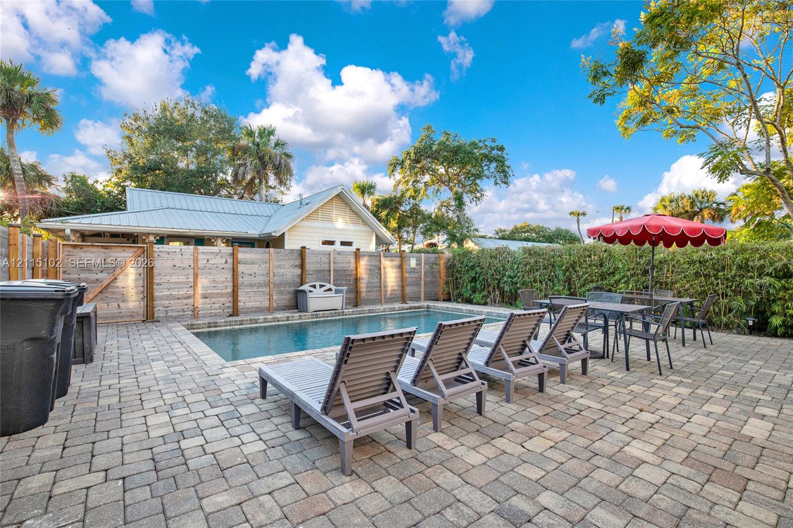 Rectangular in-ground pool featuring a paver patio, wood-slat privacy fencing, and mature perimeter landscaping
