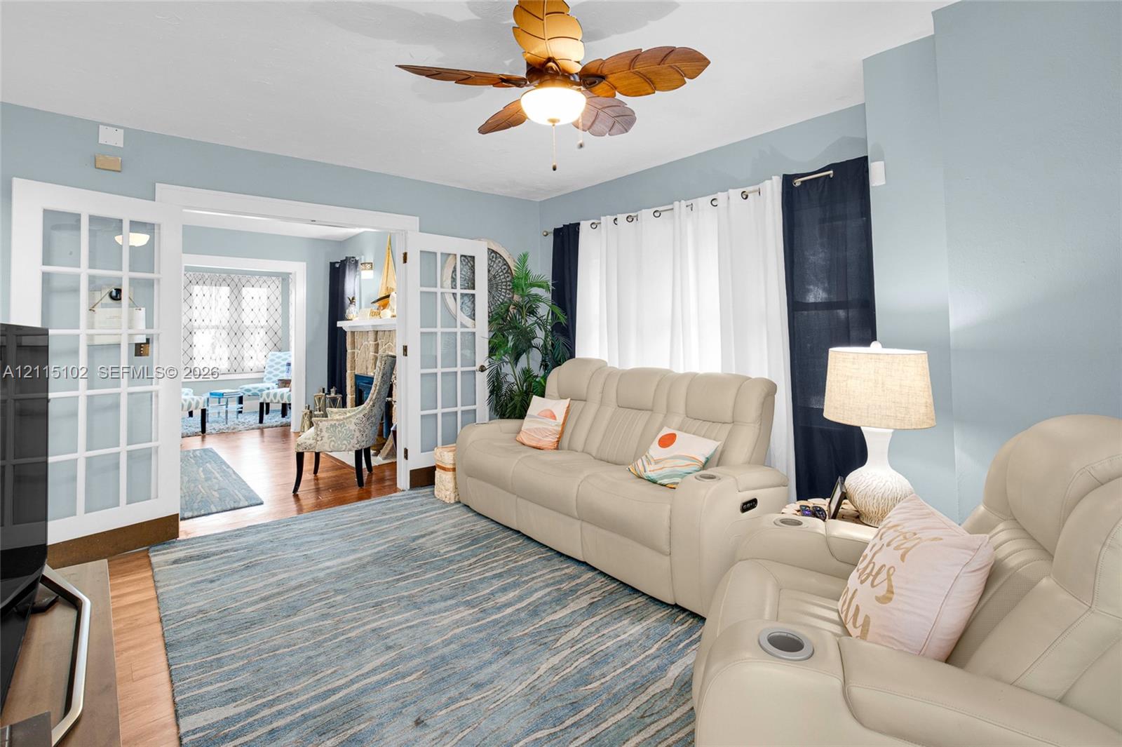 Interior space featuring double French doors, wood-finish flooring, a decorative ceiling fan with integrated lighting, and a fireplace with textured masonry surround