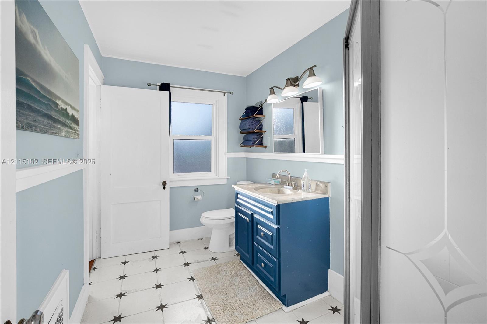 Bathroom featuring a blue vanity with a stone countertop, a single-handle faucet, a three-light fixture, and patterned tile flooring