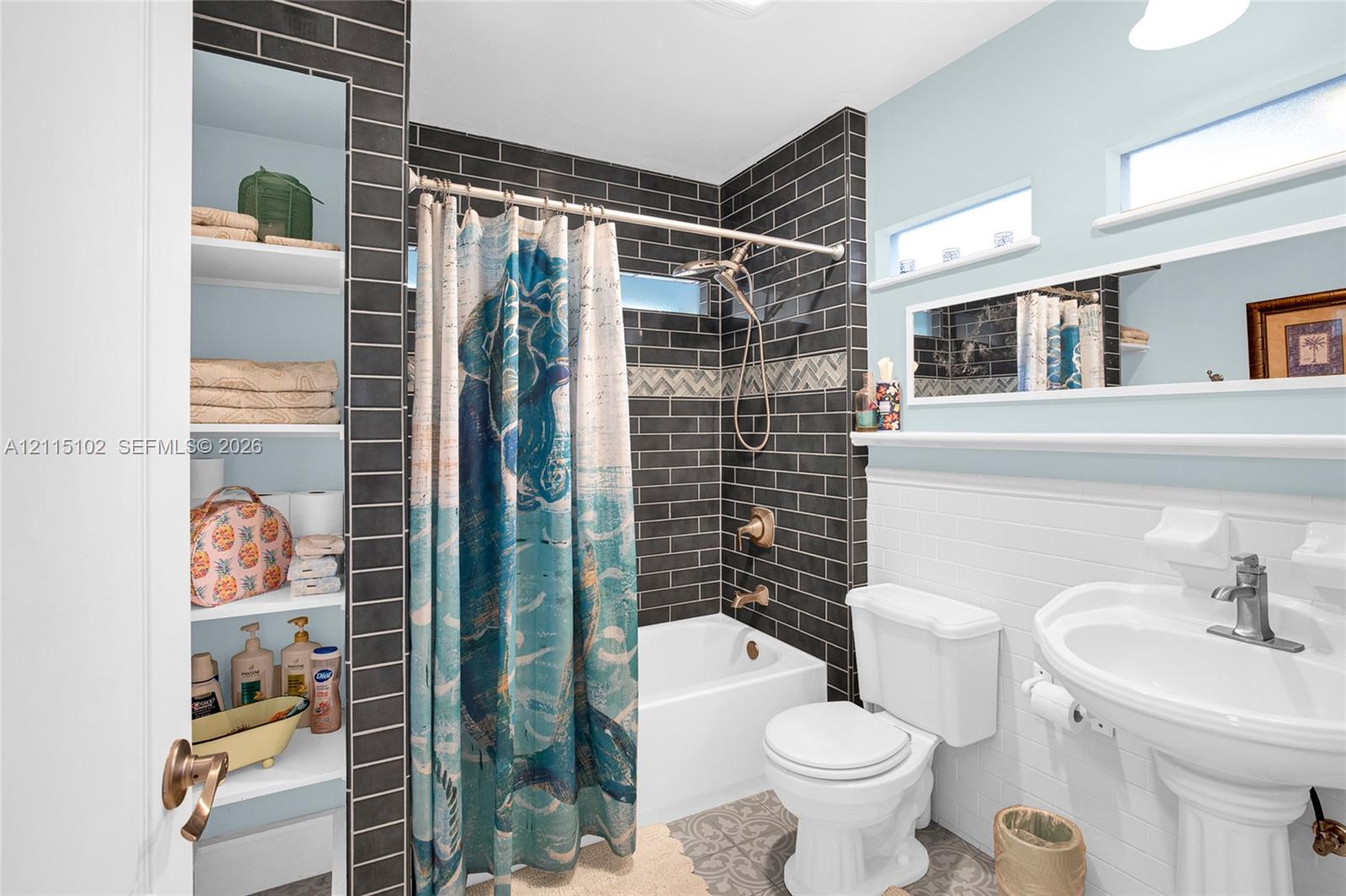 Bathroom featuring charcoal subway tile surround, integrated floor-to-ceiling built-in shelving, pedestal sink with polished metal faucet, white subway tile wainscoting, and upper horizontal windows