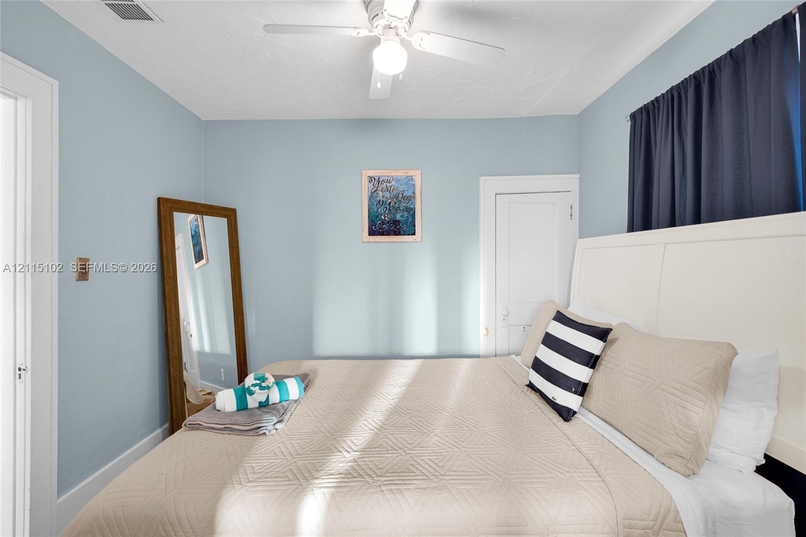 Bedroom featuring light blue walls, a white ceiling fan with integrated lighting, and a white five-panel interior door