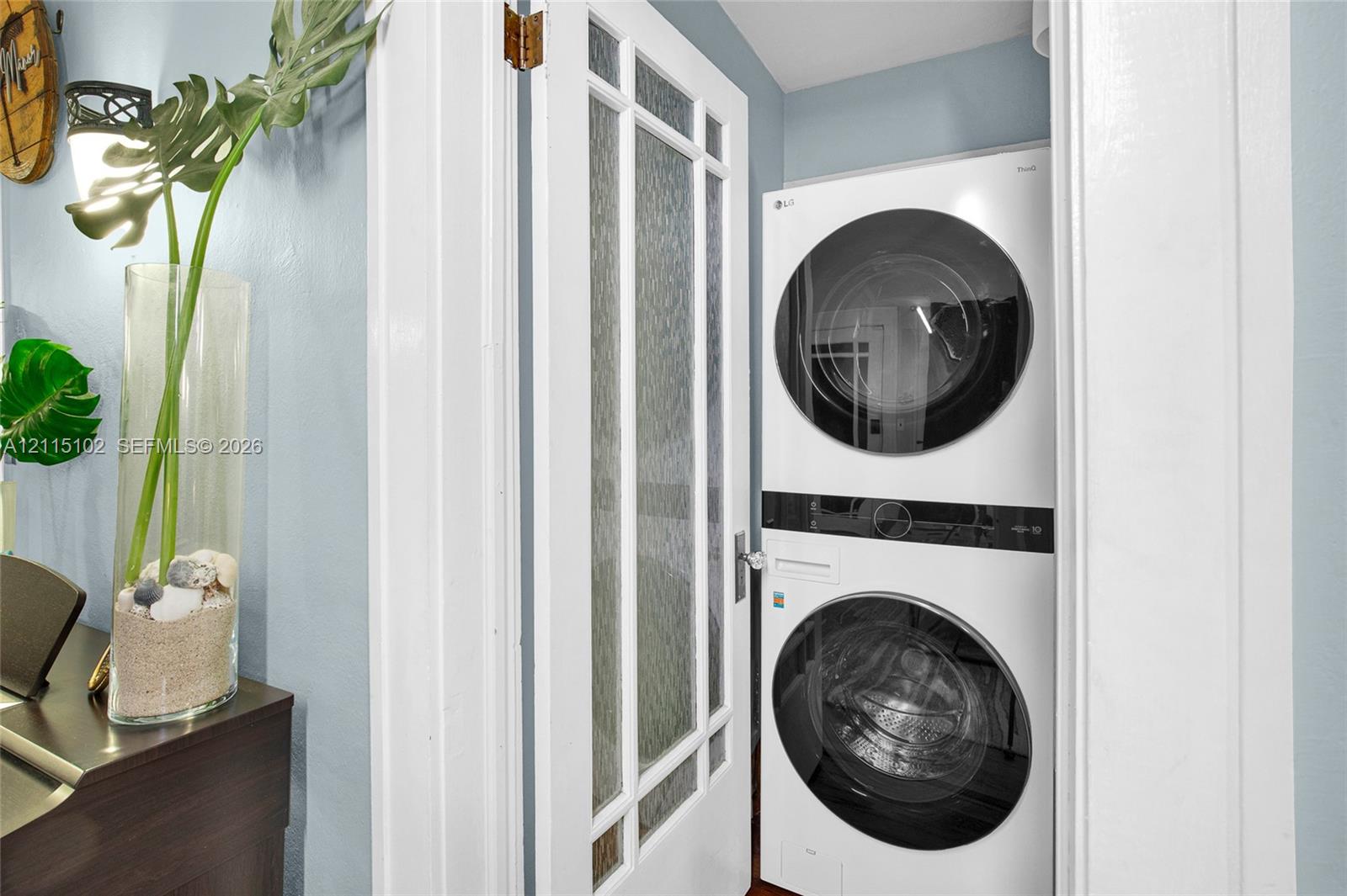 Stacked washer and dryer unit concealed behind a white door with textured glass panels