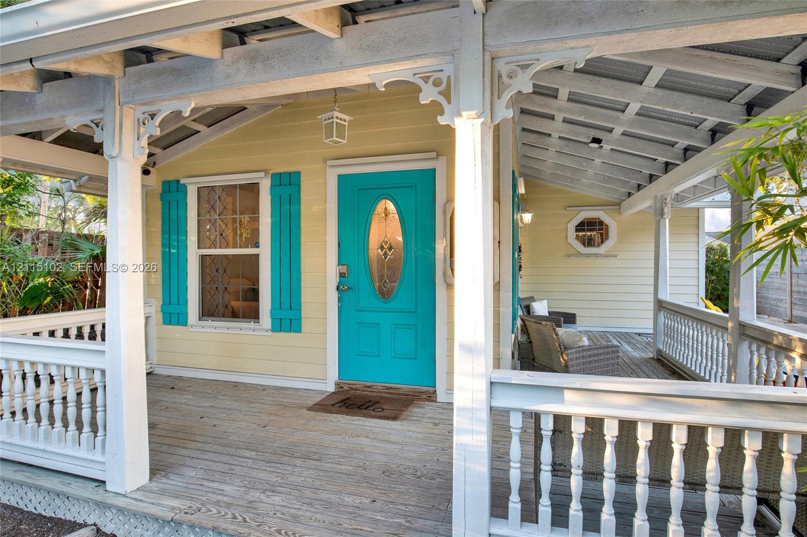 Covered wraparound porch featuring white spindle railings, decorative wooden brackets, horizontal lap siding, and a prominent entryway with a glass-inset door and contrasting shutters