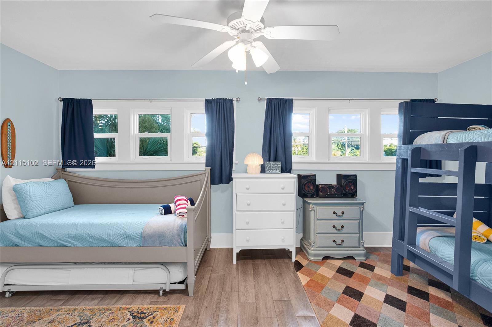 Room featuring wood-finish flooring, dual sets of triple-pane windows, and a central ceiling fan with integrated lighting