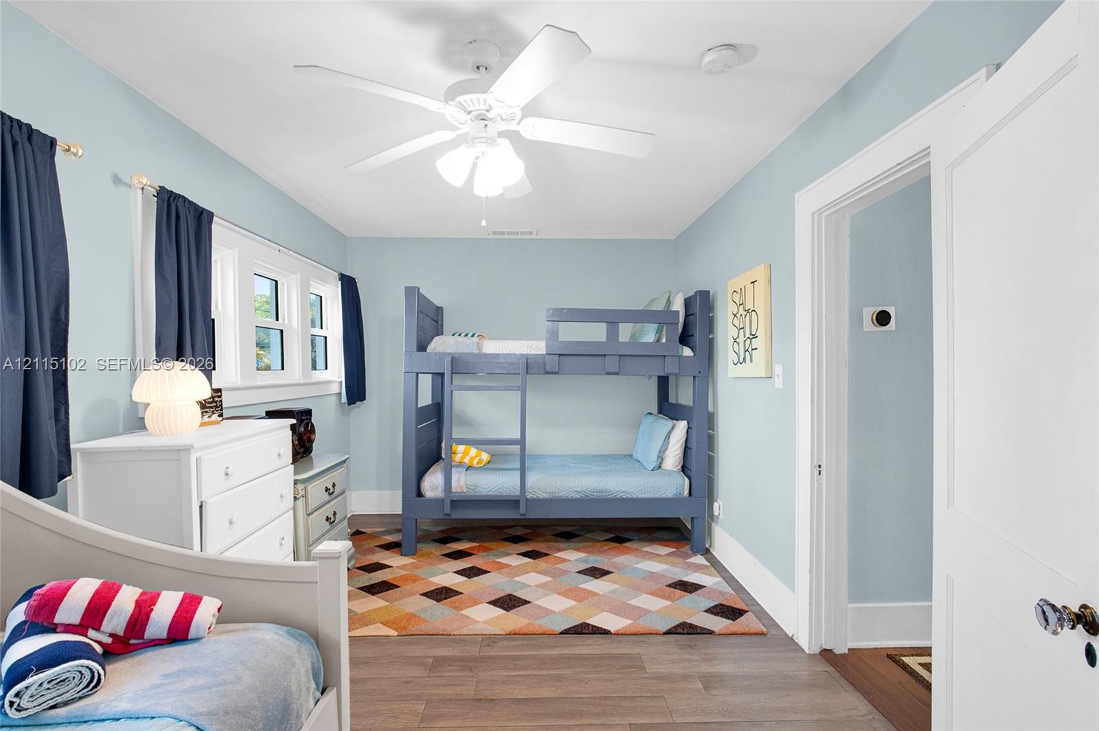 Multi-pane window assembly, white ceiling-mounted fan with integrated light fixture, wood-finish flooring, and white interior door with metallic hardware