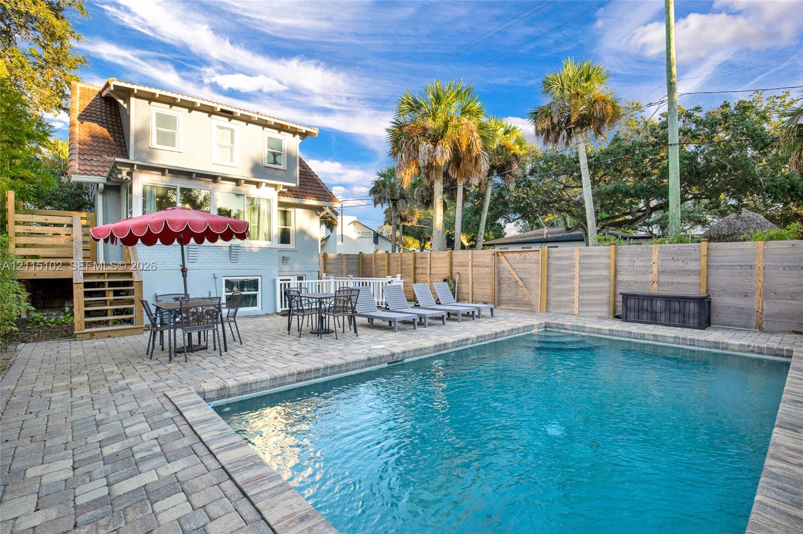 Outdoor living space featuring an in-ground swimming pool, stone paver decking, wood privacy fencing, and elevated wood-framed stairs