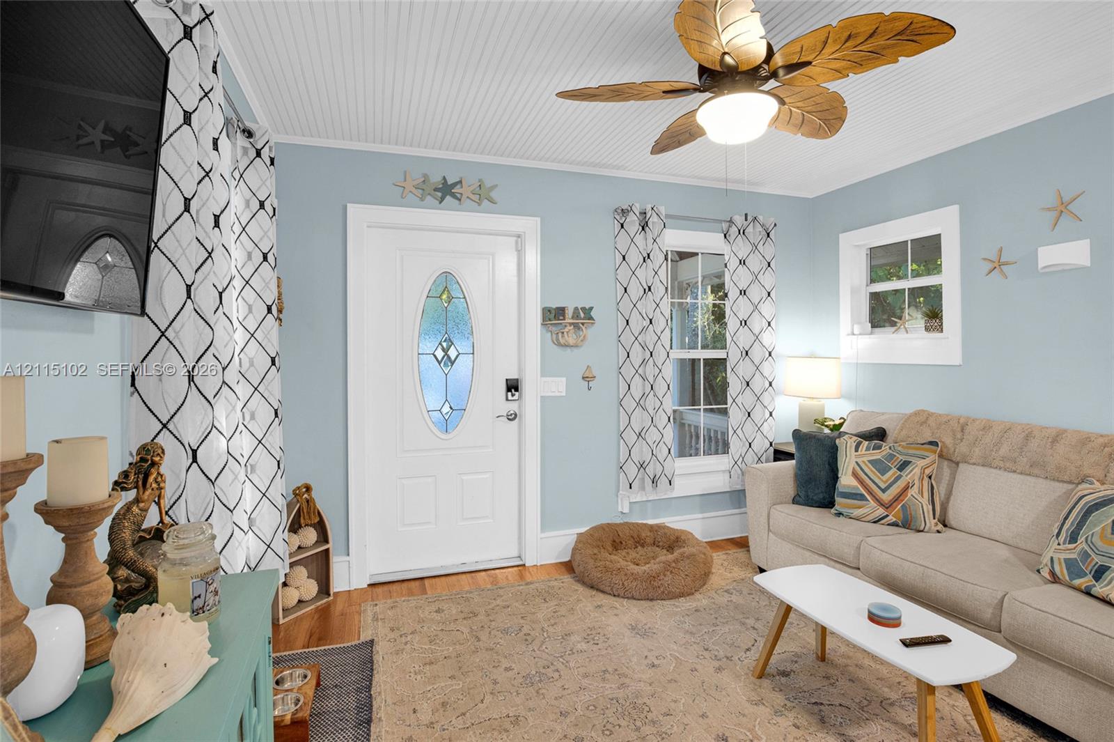 Beaded board ceiling, ceiling fan with palm-leaf blades, wood flooring, and entry door with an oval glass insert