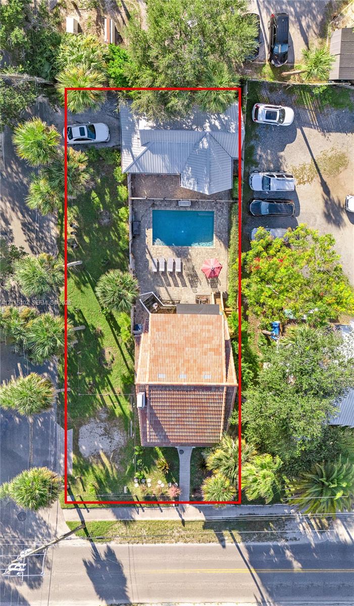 Aerial view of property featuring a swimming pool, paved patio, tiled roof, and landscaped lawn with mature palm trees