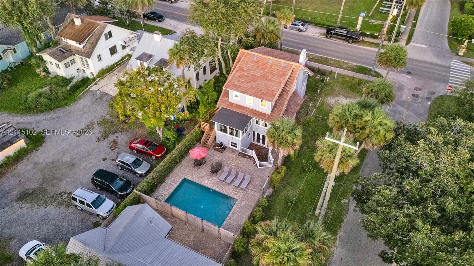 Multi-story residence featuring a shingled roof, ground-level paved patio, built-in swimming pool, and mature palm trees
