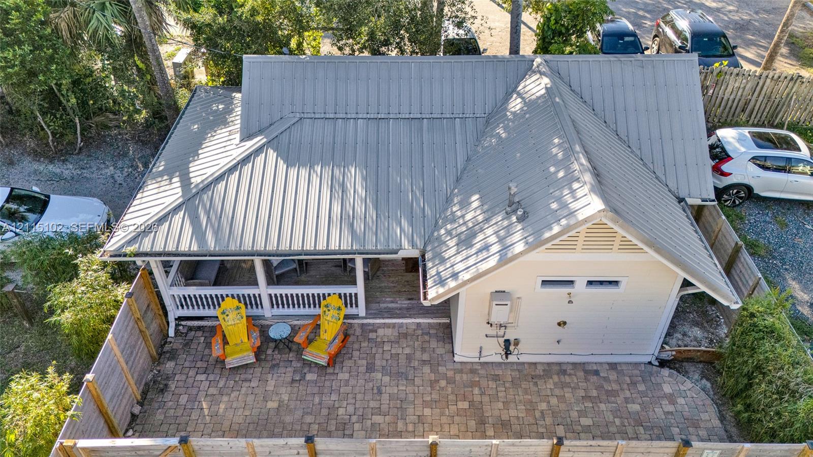 Metal roof, covered porch with white railing, and a paver stone patio enclosed by a wood privacy fence