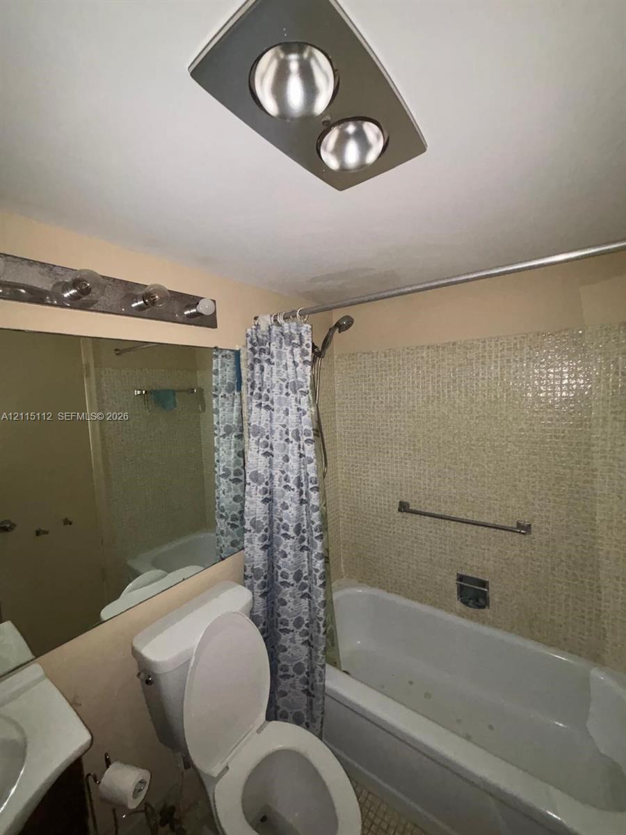 Bathroom featuring a shower-tub combination with mosaic tile surround, ceiling-mounted heating unit, and wall-mounted vanity mirror with multi-bulb light fixture