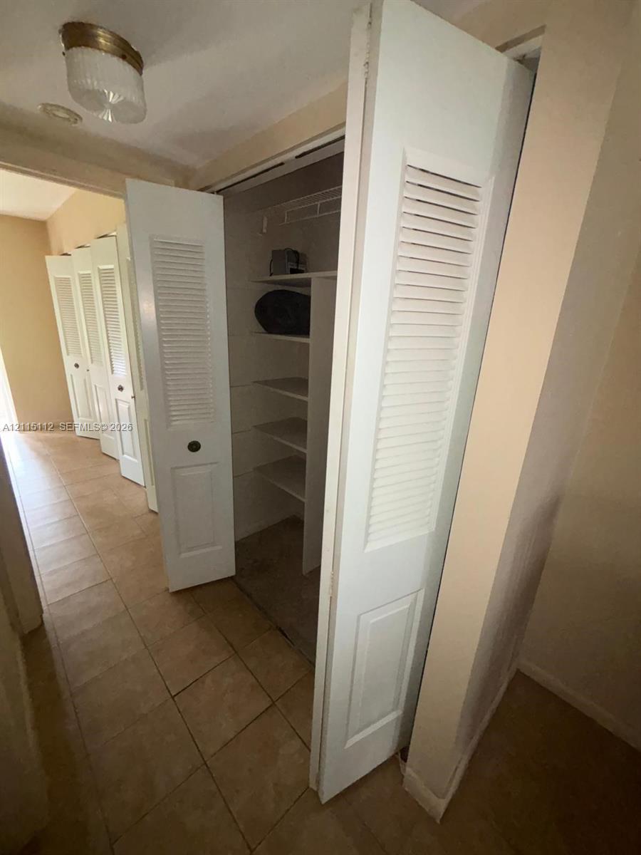 Multiple closets featuring white bi-fold louvered doors, tile flooring, and interior built-in shelving