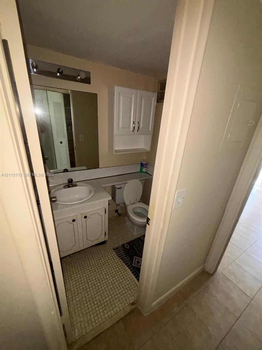 Bathroom featuring a vanity with a white cabinet and integrated sink, wall-mounted white storage cabinetry, and tiled flooring