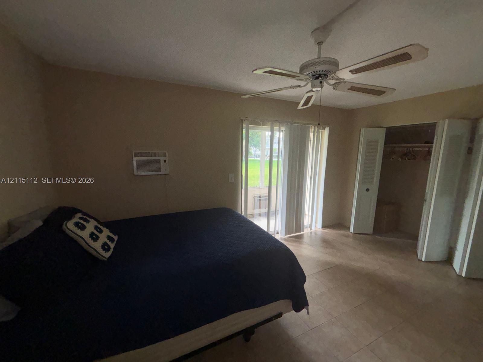 Neutral-toned room featuring tile flooring, a multi-blade ceiling fan, sliding glass doors, and a closet with bifold doors