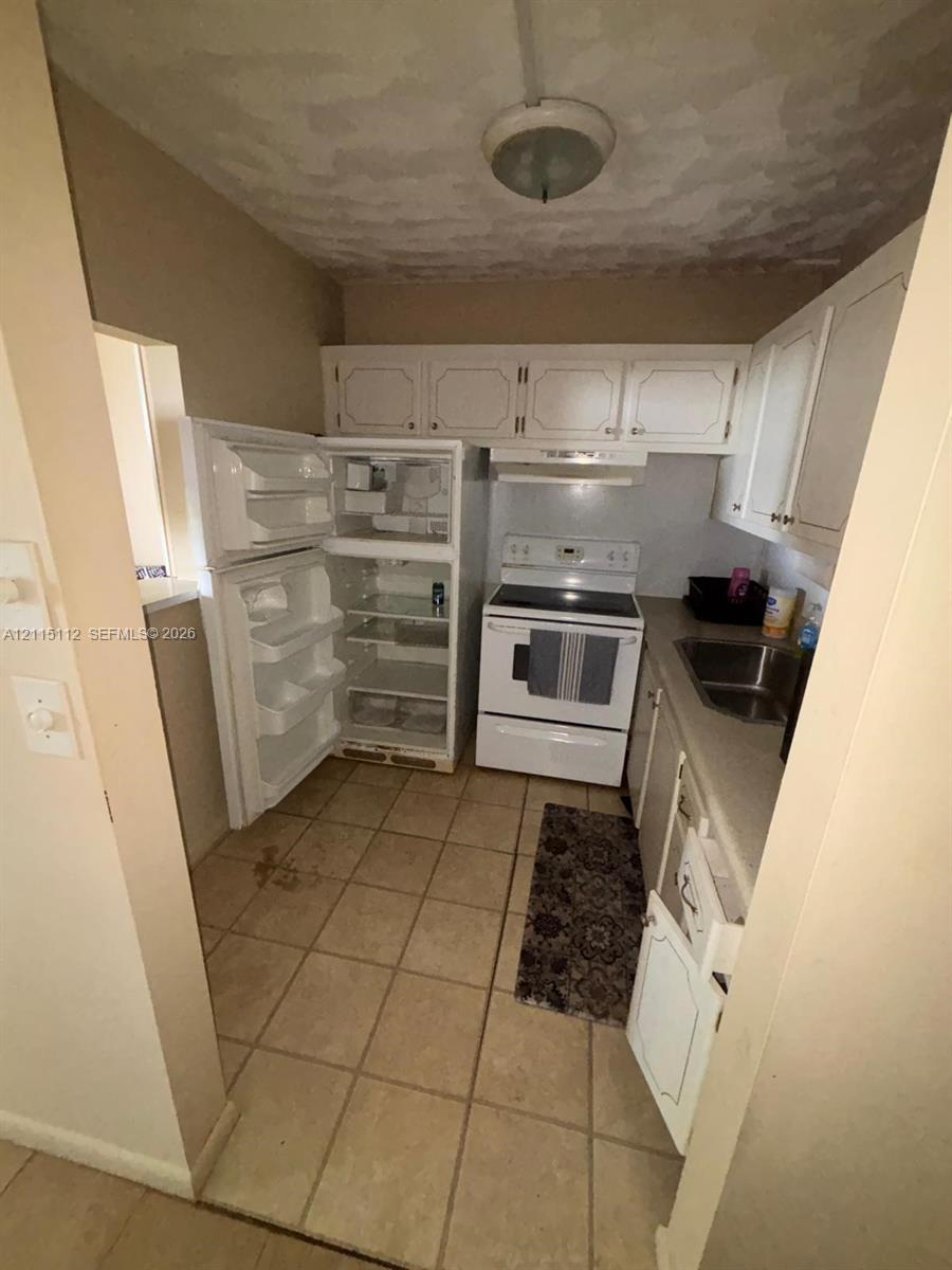 Kitchen featuring white cabinetry, tile flooring, stainless steel sink, and white electric range with integrated range hood