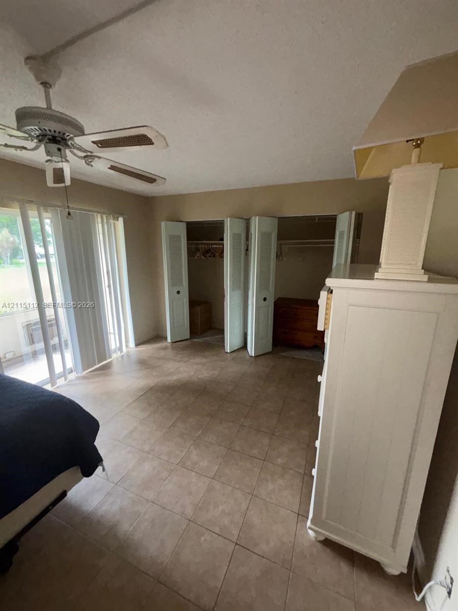 Ceramic tile flooring, built-in closet with bi-fold louvered doors, ceiling fan with integrated light fixture, and floor-to-ceiling sliding glass doors