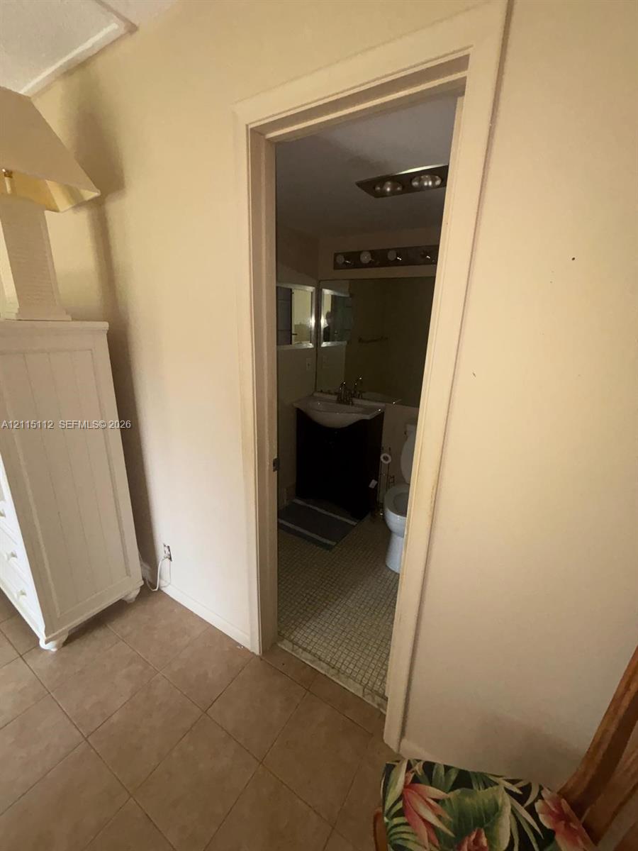 Bathroom featuring a dark-finish vanity with a white basin, a wall-mounted light fixture, and tile flooring