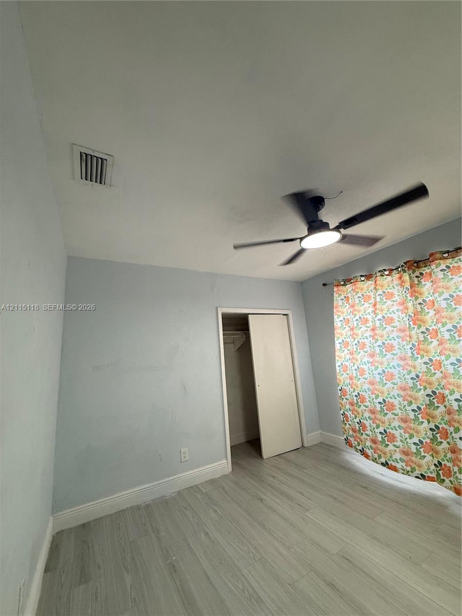 Room featuring wood-finish flooring, a matte black ceiling fan with integrated lighting, and a closet with a swinging door