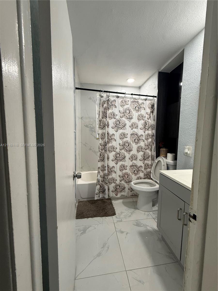 Bathroom featuring large-format tile flooring with a marble-finish, a grey vanity cabinet, and a shower-tub combination with tile surround