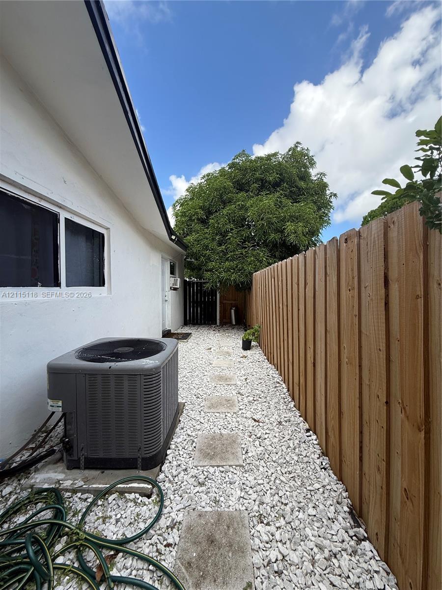Side yard exterior featuring a vertical wood privacy fence, white stone ground cover, stone pavers, and a mounted central air conditioning unit