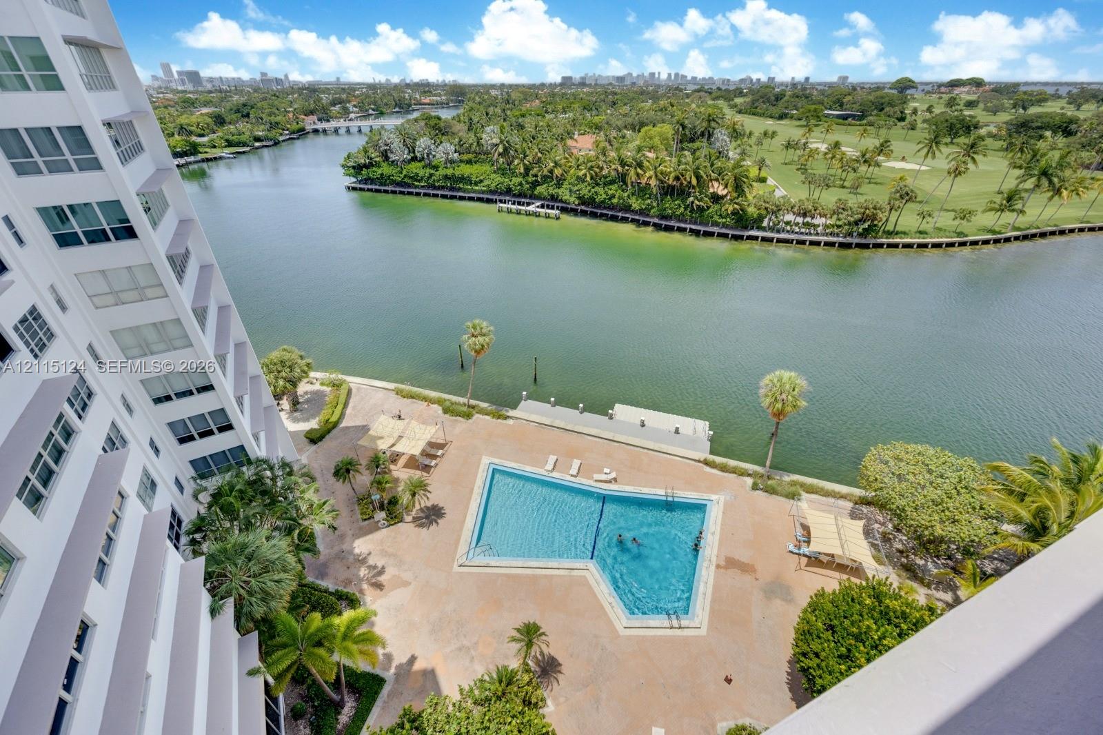 Aerial perspective of the property grounds featuring a swimming pool, paved deck, water frontage, and lush landscaping Aerial perspective of the property grounds featuring a swimming pool, paved deck, water frontage, and lush landscaping