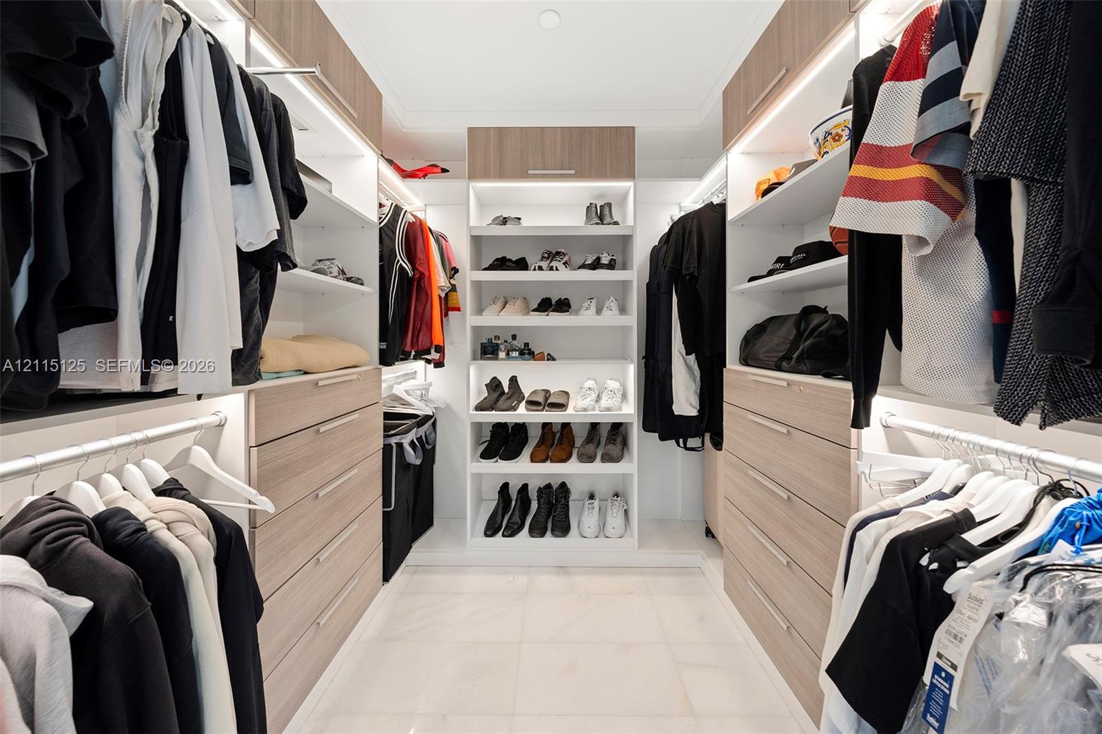 Custom walk-in closet featuring light wood-finish cabinetry, floor-to-ceiling shelving, integrated LED accent lighting, and large-format tile flooring