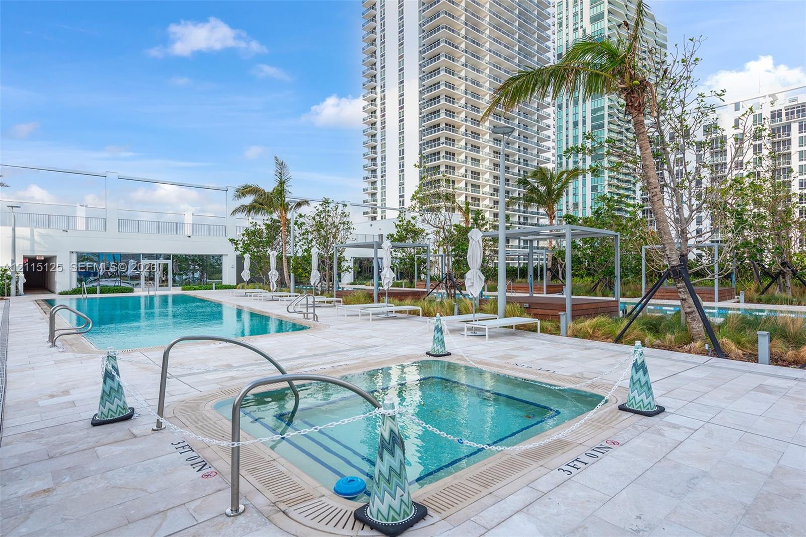 Swimming pool and spa area featuring natural stone deck surfacing, integrated metal handrails, and surrounding palm tree landscaping