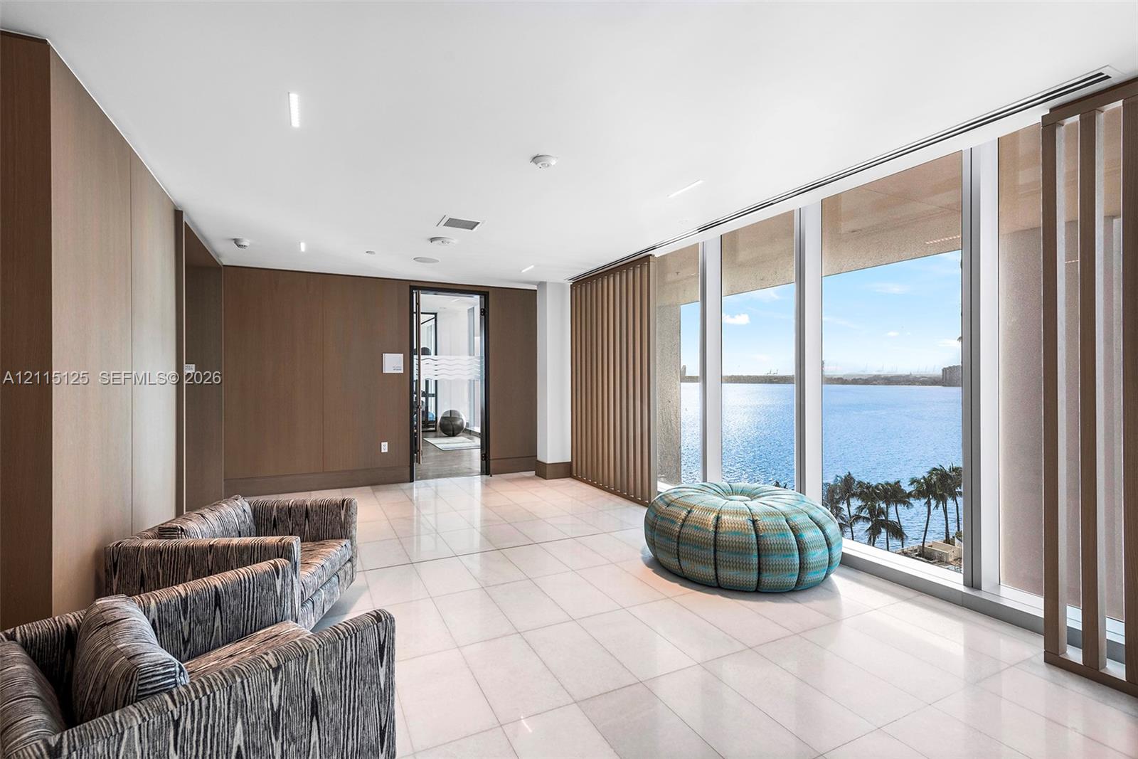Interior space featuring full-height wood-panel walls, polished tile flooring, recessed ceiling lighting, and floor-to-ceiling windows with water scenery