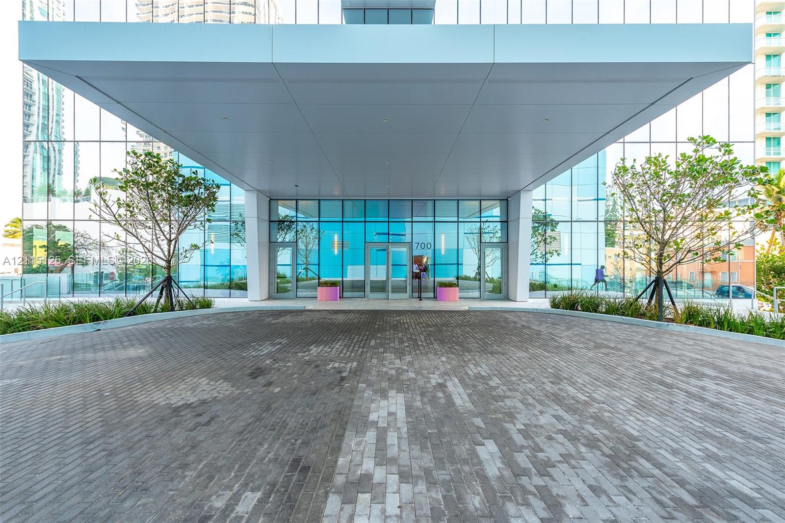 Grand porte-cochre entrance featuring a geometric cantilevered canopy, floor-to-ceiling glass curtain wall facade, and paved motor court
