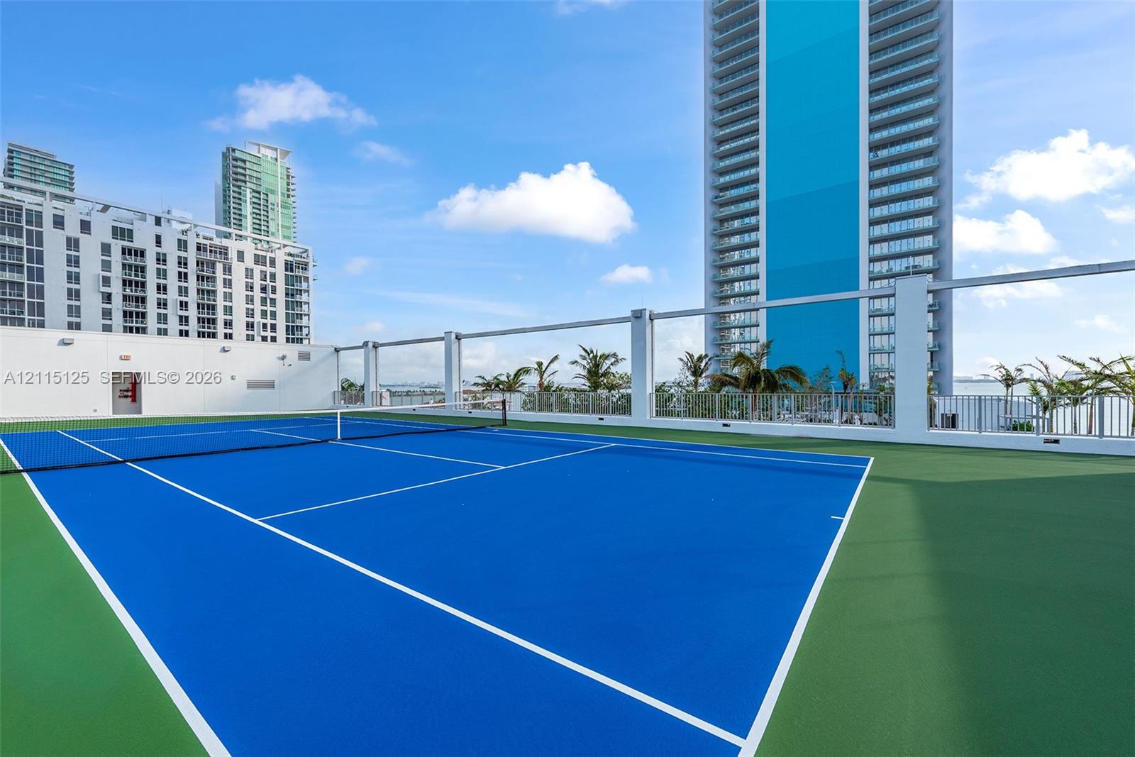 Rooftop tennis court featuring a blue and green multi-surface finish and a white perimeter railing