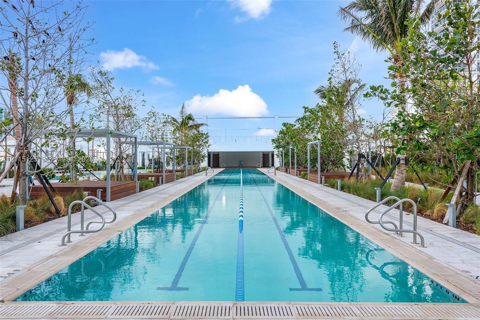 Lap pool featuring dual entry rails, perimeter stone decking, and custom wood-finished cabanas nestled among mature landscaping