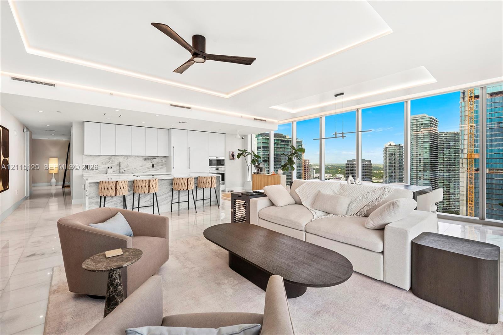 Open-concept living space featuring floor-to-ceiling windows, recessed tray lighting, stone-finish flooring, a modern three-blade ceiling fan, and a kitchen equipped with integrated cabinetry and a stone-pattern backsplash