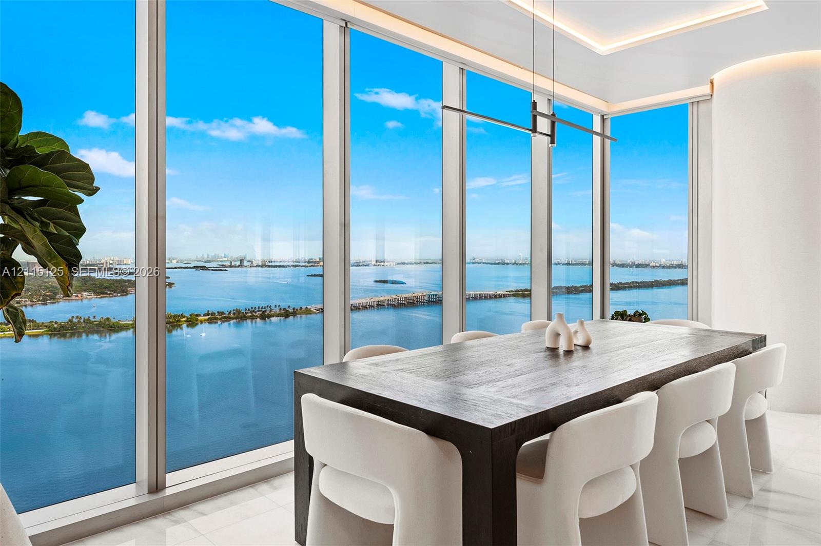 Floor-to-ceiling windows, water backdrop, stone flooring, and recessed ceiling lighting with perimeter cove detail