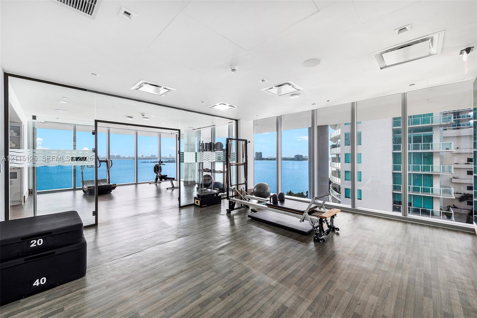 Fitness space featuring floor-to-ceiling glass walls, wood-finish flooring, recessed lighting, and expansive water exposure