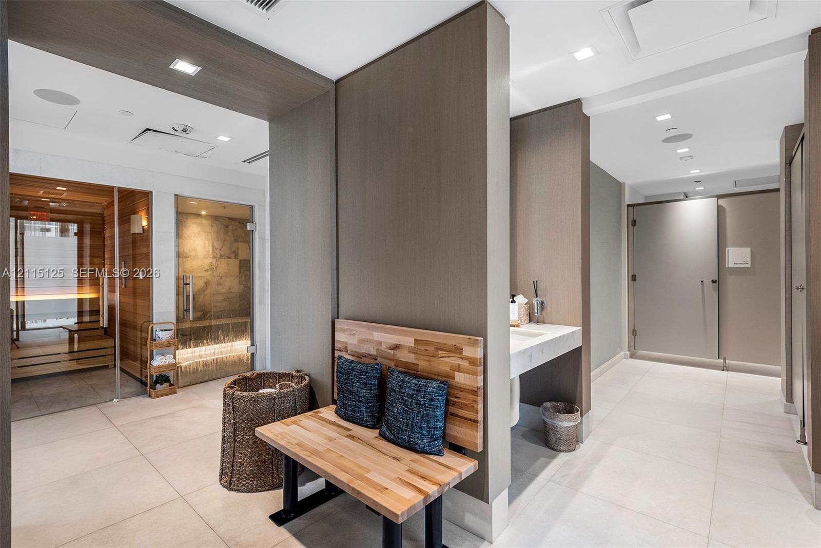 Spa-inspired room featuring a glass-enclosed sauna with tiered wood seating, a separate glass-walled steam shower, large-format tile flooring, and integrated wall-mounted sinks with stone-finish surfaces